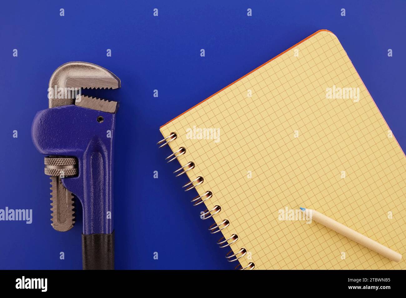 Verstellbarer Rohrschlüssel und offenes Notizbuch mit Draht auf blauem Hintergrund, Sanitär- und mechanisches Schätzkonzept mit freiem Platz für Text Stockfoto