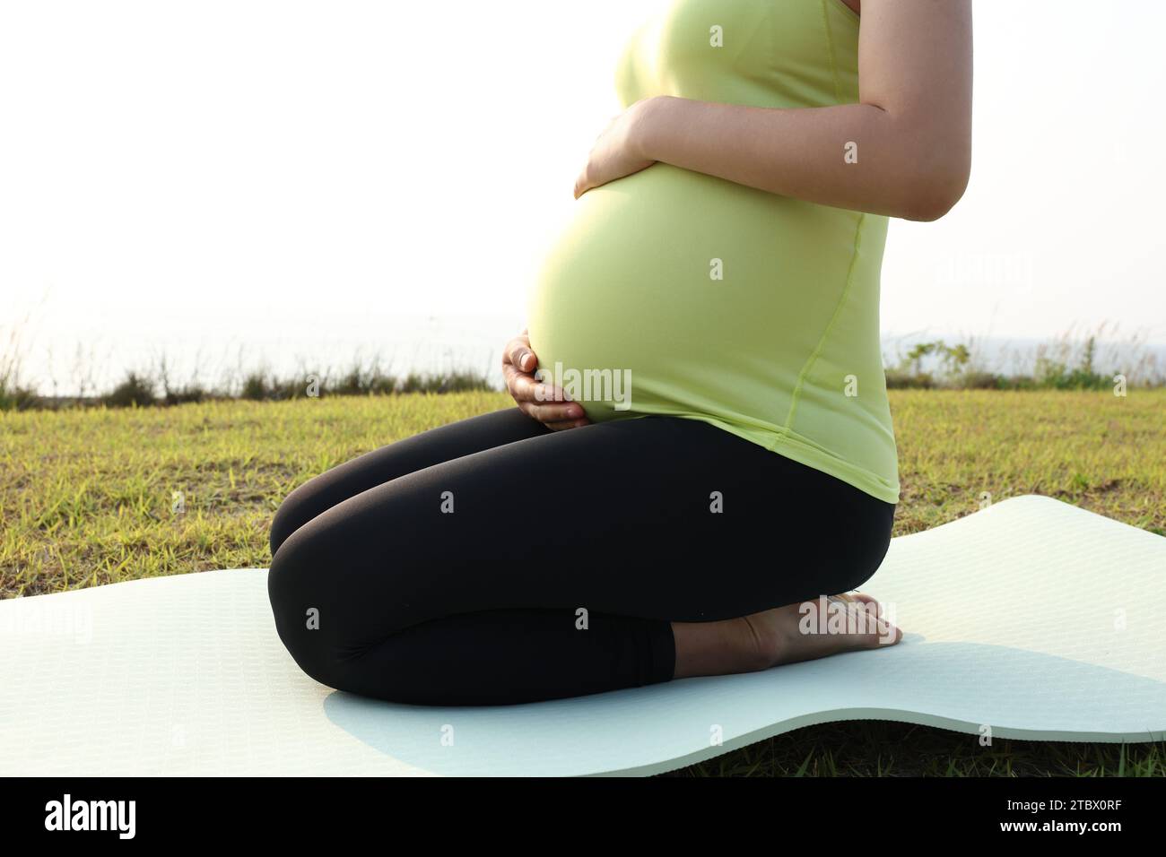 Schwangere Frau, die Yoga-Posen für Meditation am Strand macht Stockfoto