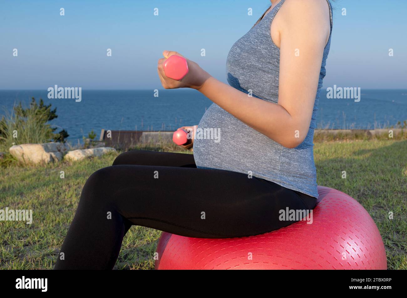 Eine schwangere Frau trainiert auf einem Fitnessball am Strand Stockfoto