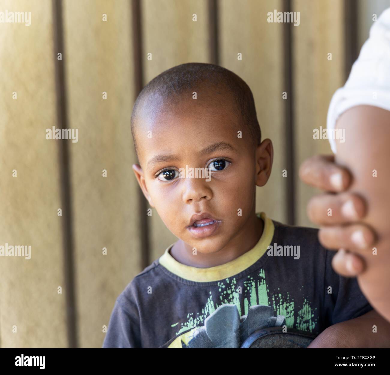 afrikanisches Kleinkind mit rasiertem Kopf vor dem Haus Stockfoto