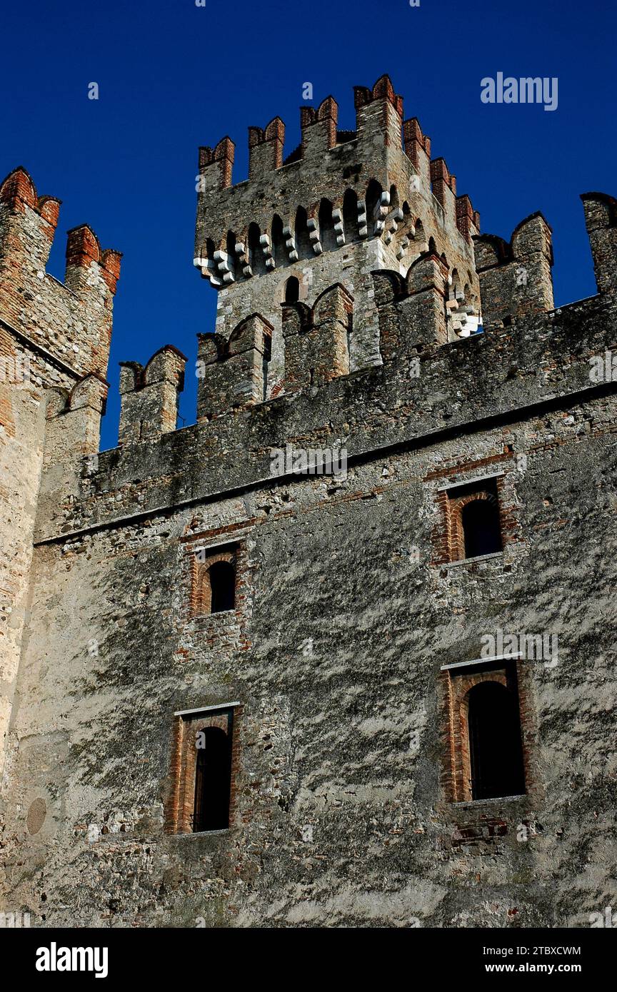 Ein 29 Meter hoher Turm mit Schwalbenschwanz-Zinnen, die für mittelalterliche Bogenschützen und Machicolationen oder „Mordlöcher“ zum Abwerfen von heißem Öl oder Felsbrocken auf Angreifer ausgelegt sind, schwingt über dem Castello Scaligero oder der Rocca Scaligera in Sirmione am Gardasee in der Lombardei, Italien. Die Burg wurde in den 1300er Jahren erbaut und hat ihren Namen von der Familie Della Scala, der Herrscherin in Verona, die das Gebiet zu dieser Zeit dominierte. Es ist eine der am besten erhaltenen Scaliger-Festungen. Stockfoto