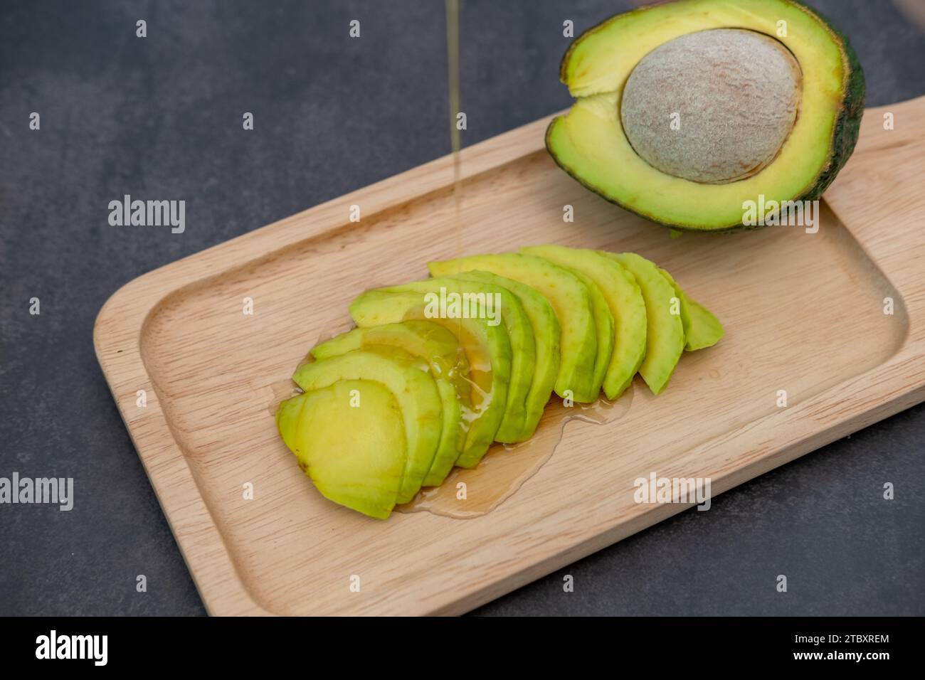 Blick von oben auf geschnittene und halbierte Avocado, auf der Honig auf schwarzem Hintergrund fließt Stockfoto