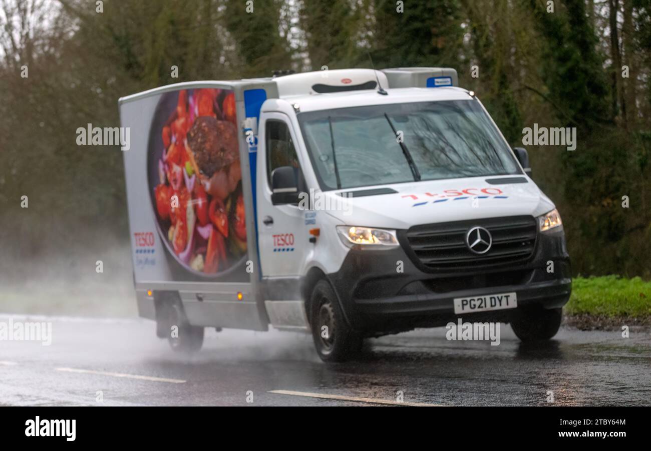 Milton Keynes, Bucks, UK - 9. Dezember 2023: 2021 Mercedes Benz Sprinter Transporter für Tesco-Heimlieferungen auf nasser Straße, im Regen mit Kopflicht Stockfoto