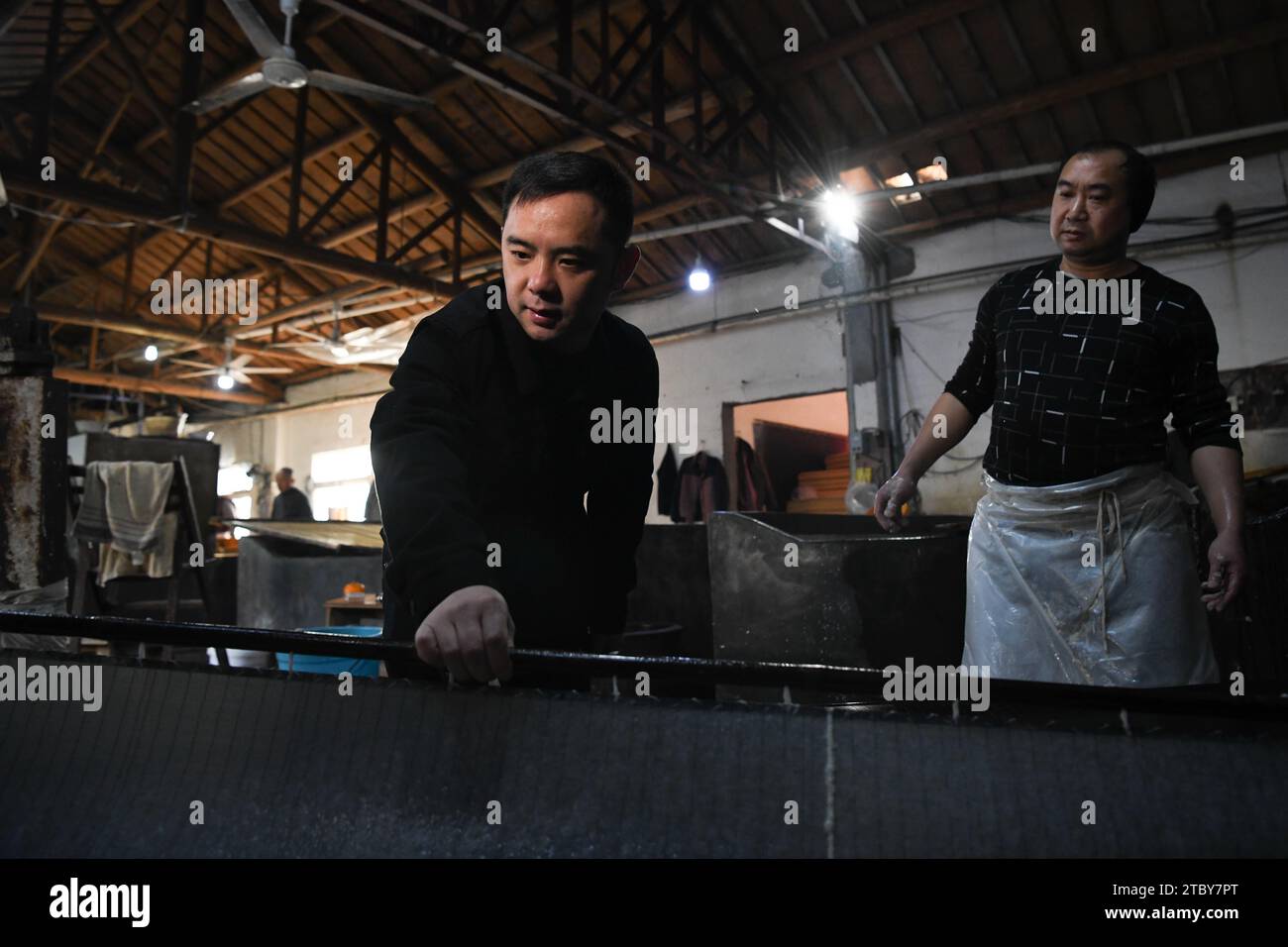 (231209) -- JINGXIAN, 9. Dezember 2023 (Xinhua) -- Li Chao (L) sammelt Papierzellstoff in der Werkstatt eines Unternehmens in Jingxian County, ostchinesischer Provinz Anhui, 8. Dezember 2023. Xuan Papier, das auf die Tang-Dynastie (618-907) zurückgeht, hat eine Geschichte von über 1.000 Jahren. Die Zeitung stammt aus dem Komitat Jingxian (verwaltet von „Xuanzhou“ in der Tang-Dynastie) in der ostchinesischen Provinz Anhui und erhielt ihren Namen, nachdem sie als Tribut an den Kaiser geschickt wurde. Aus Strohhalmen aus Gezeitengebieten und Schalen von Wingceltis in der Nähe von Jingxian County als Material wird das Papier auf traditionelle Weise hergestellt, um einem Künstler mit hohem Standard zu dienen Stockfoto