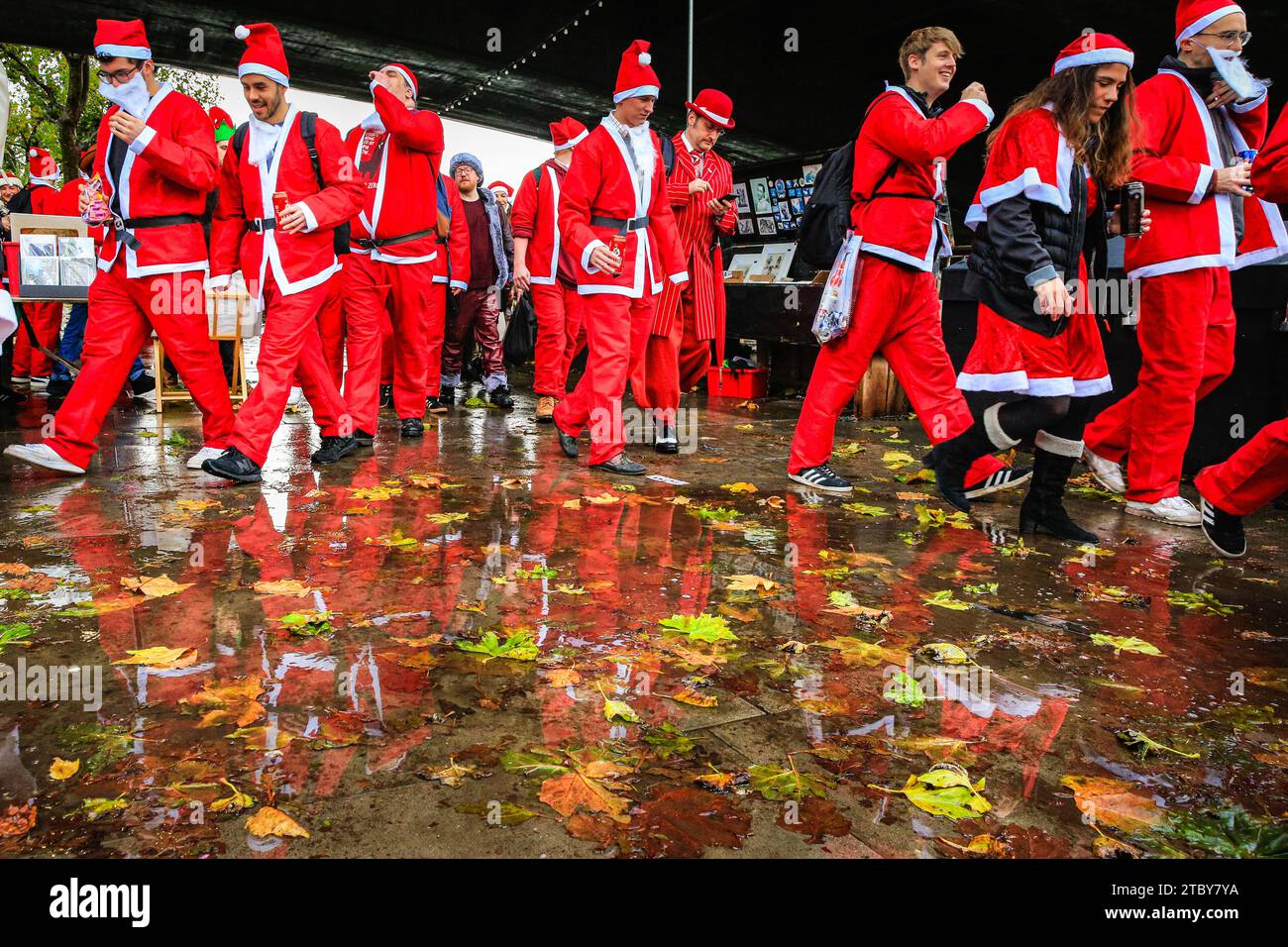 London, Großbritannien. Dezember 2023. Die santas spiegeln sich in Pfützen entlang der South Bank wider. Hunderte von Teilnehmern in santa-Outfits haben Spaß bei der jährlichen SantaCon London Christmas Parade. Das Get Together, das gemeinnützig ist und auch für wohltätige Zwecke einsammelt, sieht die fröhlichen weihnachtsfeier einen Spaziergang von der Leake Street in Waterloo durch Teile Londons und endet am Abend am Trafalgar Square, wo sie verschiedene Pub-Haltestellen und Sehenswürdigkeiten entlang der Strecke besichtigen. Quelle: Imageplotter/Alamy Live News Stockfoto