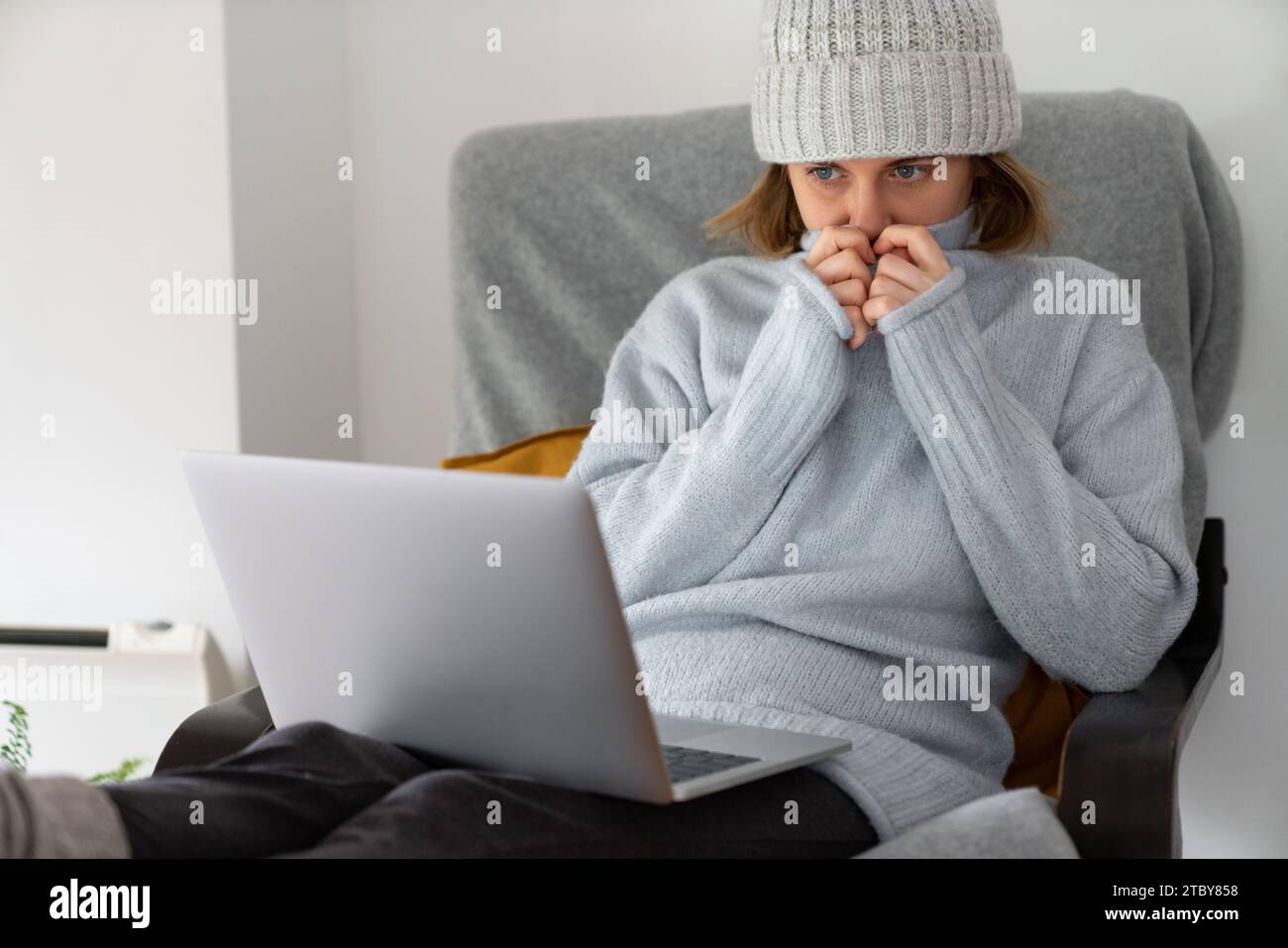 Eine Frau in warmen Kleidern mit Laptop. Niedrige Heiztemperatur im Haus. Energiekrise-Konzept. Stockfoto