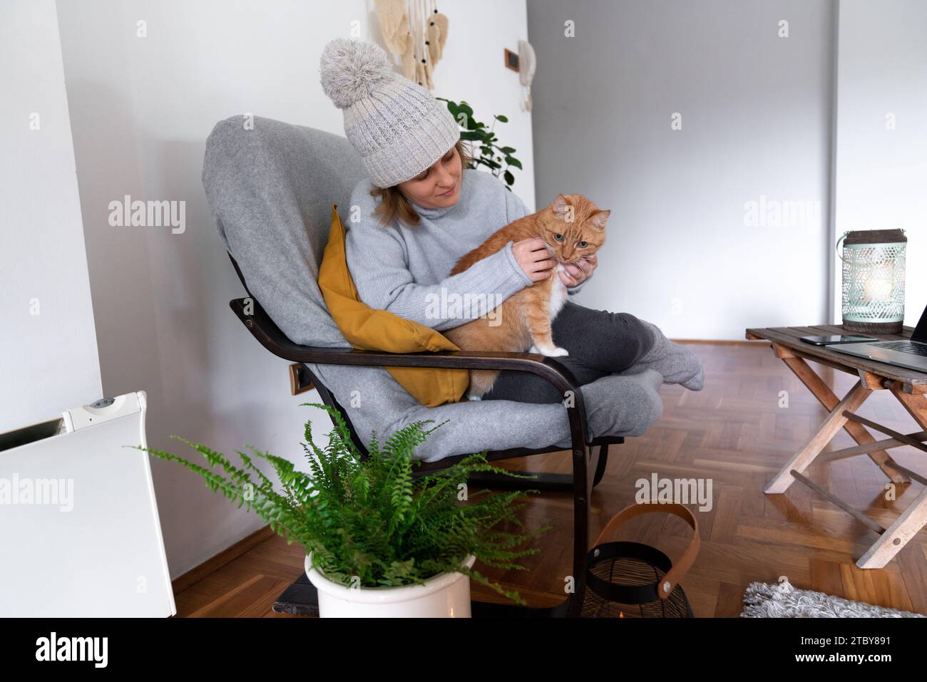Eine Frau in warmen Kleidern mit Laptop. Niedrige Heiztemperatur im Haus. Energiekrise-Konzept. Stockfoto