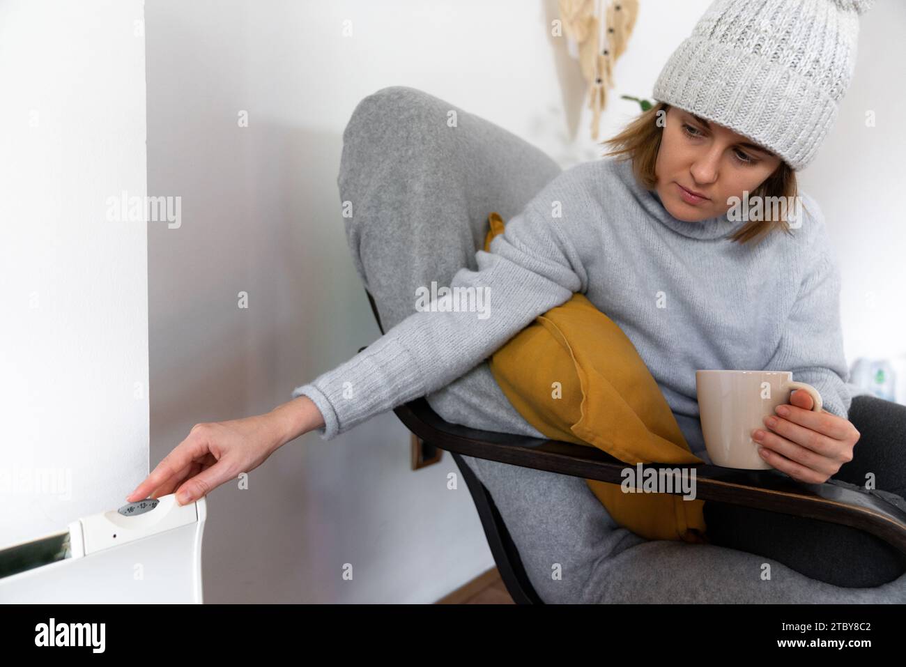 Eine Frau in warmen Kleidern hält ihre Hand auf dem Heizungsthermostat. Niedrige Heiztemperatur im Haus. Energiekrise-Konzept. Stockfoto