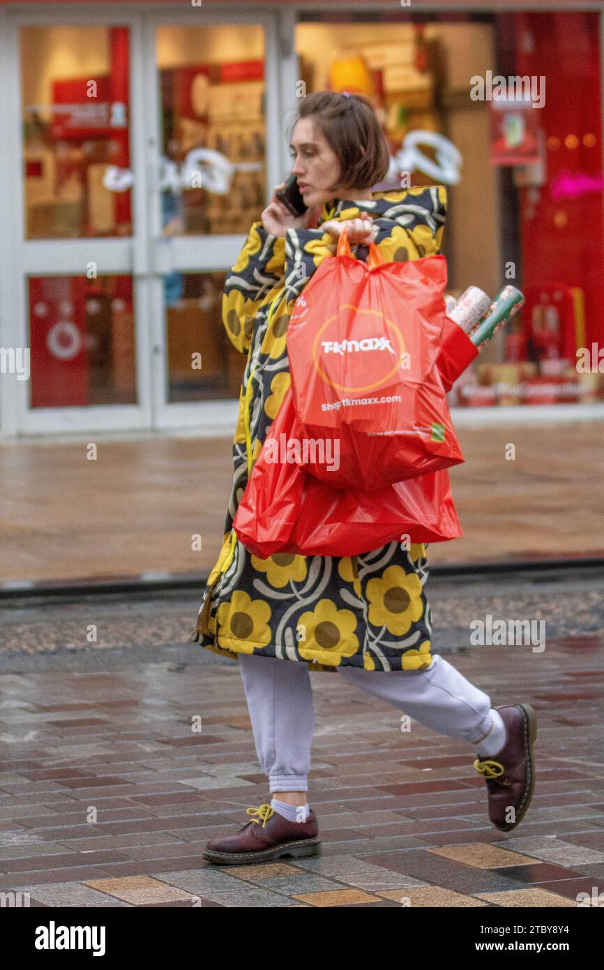 Frau mit hellem Sonnenblumenmantel, feierliche Einkäufe in Preston, Großbritannien. Dezember 2023. Weihnachtsläden, Shopper, Einkaufen an einem nassen Tag in der Fishergate High Street. Stockfoto