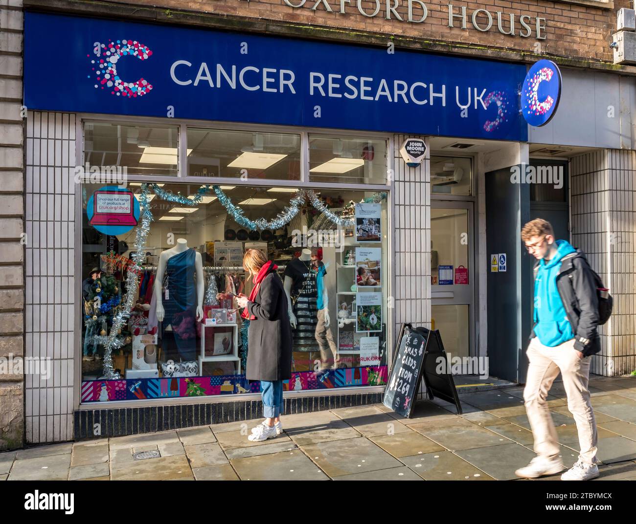 Frau, die ein Mobiltelefon außerhalb des Cancer Research UK-Shops benutzt, High Street, Lincoln City, Lincolnshire, England, UK Stockfoto