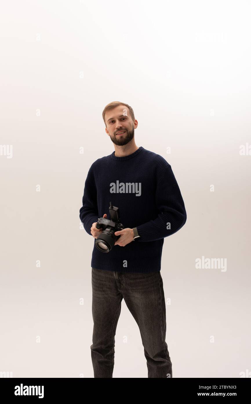 Hübscher, lächelnder junger Fotograf, der im Studio eine professionelle Digitalkamera über weißem Hintergrund hält. Stockfoto