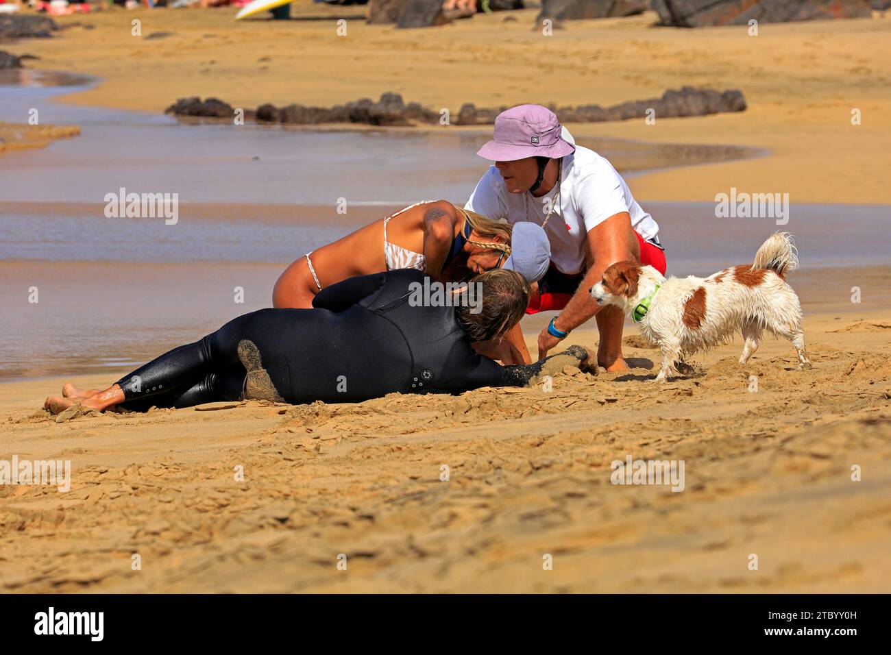 Rettungsschwimmer hilft einem verletzten Surfer mit besorgtem Hund in El Cotillo, Fuerteventura, Kanarischen Inseln, Spanien. Vom November 2023 Stockfoto