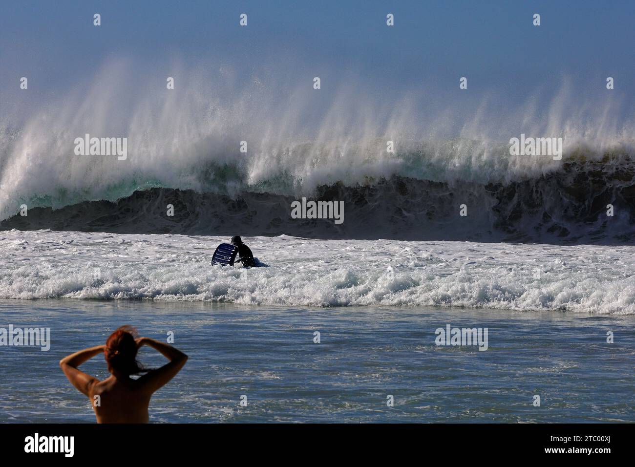 Eine Frau, die auf das Meer blickt, und sieht besorgt aus, wie ein Freund in wilden Wellen auf El Cotillo, Fuerteventura, den Kanarischen Inseln, Spanien surft. November 2023. Stockfoto