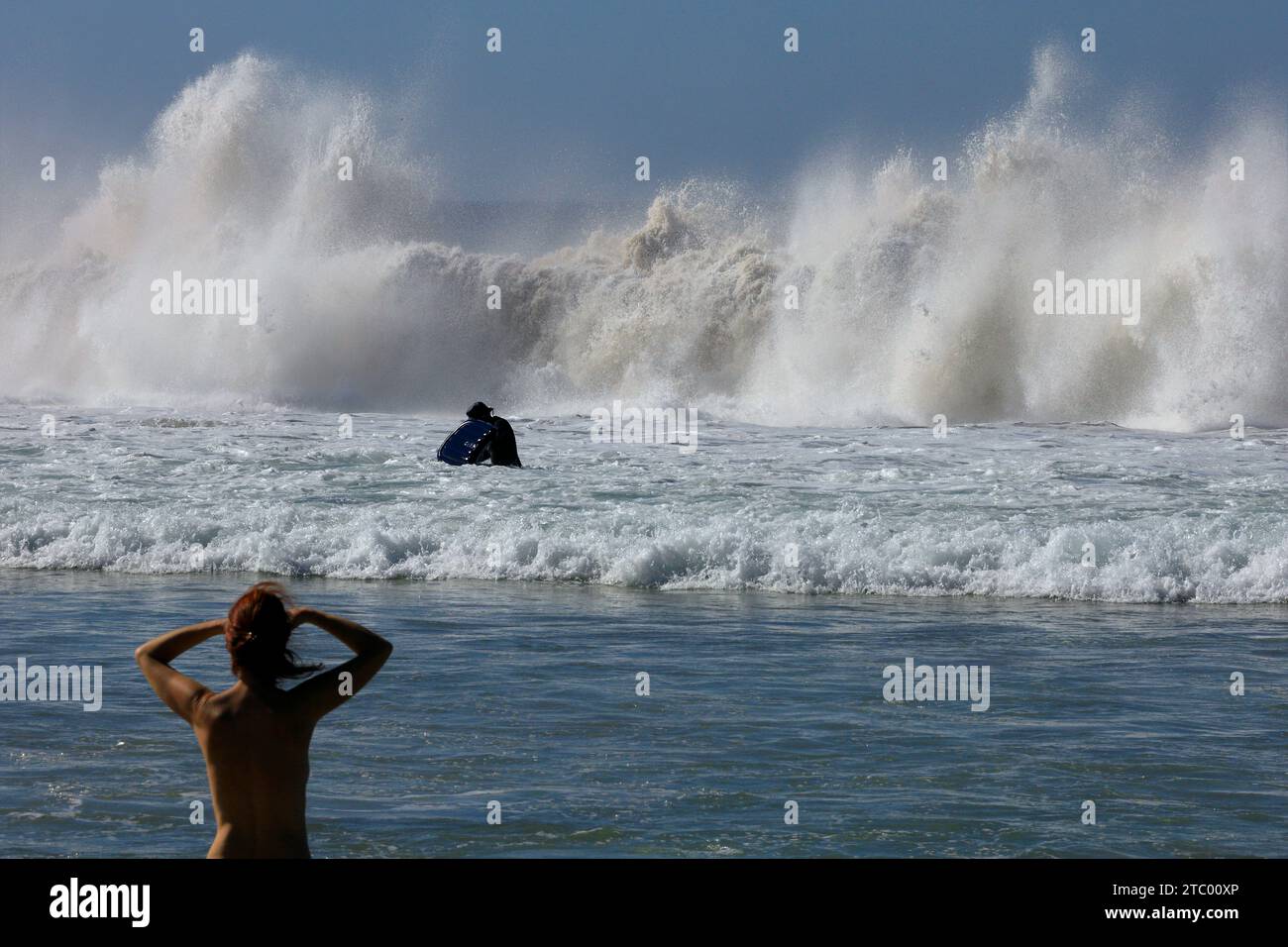 Eine Frau, die auf das Meer blickt, scheint besorgt zu sein, dass ihre Freundin in wilden Wellen auf El Cotillo, Fuerteventura, den Kanarischen Inseln, Spanien surft Stockfoto
