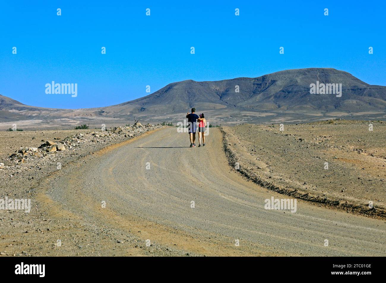 Paare, die in die Ferne gehen, in Richtung der Berge auf einem staubigen Pfad, El Cotillo, Fuerteventura, Kanarischen Inseln, Spanien. Vom November 2023. Stockfoto