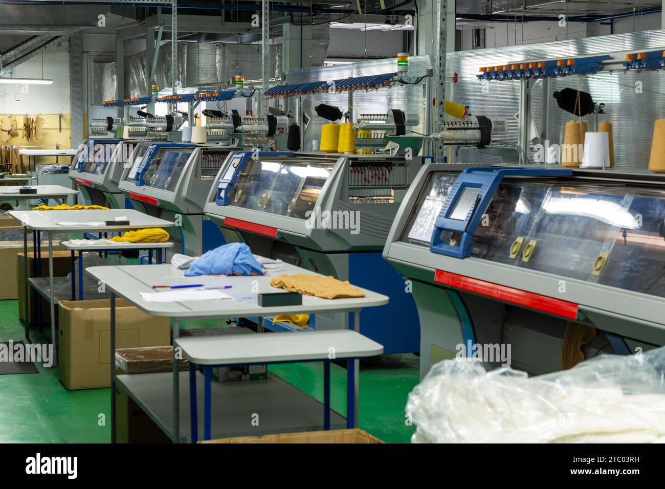Eine Reihe industrieller Textil-Flachstrickmaschinen in einer Strickfabrik. Eine industrielle Linie moderner Strickautomaten, die in zwei Reihen angeordnet sind Stockfoto
