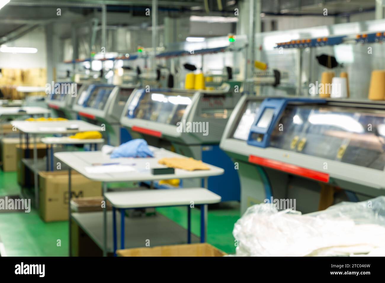 Verschwommenes Bild industrieller Textil-Flachstrickmaschinen in einer Strickfabrik. Eine industrielle Linie moderner Strickautomaten. Stockfoto