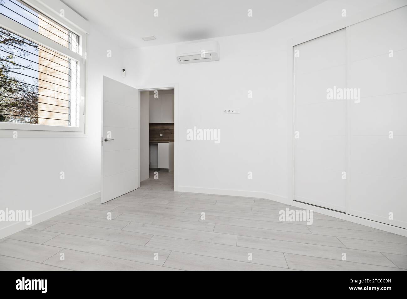 Ein leerer Raum mit Erkerfenster in einem Haus im Loft-Stil mit einem zweigeteilten Einbauschrank mit weißen Holzschiebetüren Stockfoto