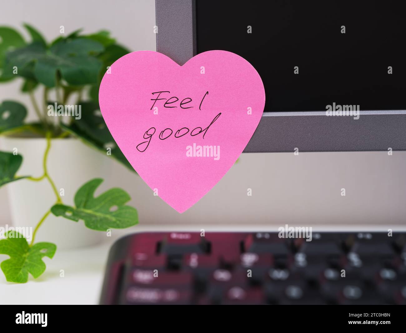 Ein rosafarbener, herzförmiger Papierschein mit Worten, die sich gut anfühlen, ist an einem Arbeitsplatz am Monitor angebracht. Stockfoto