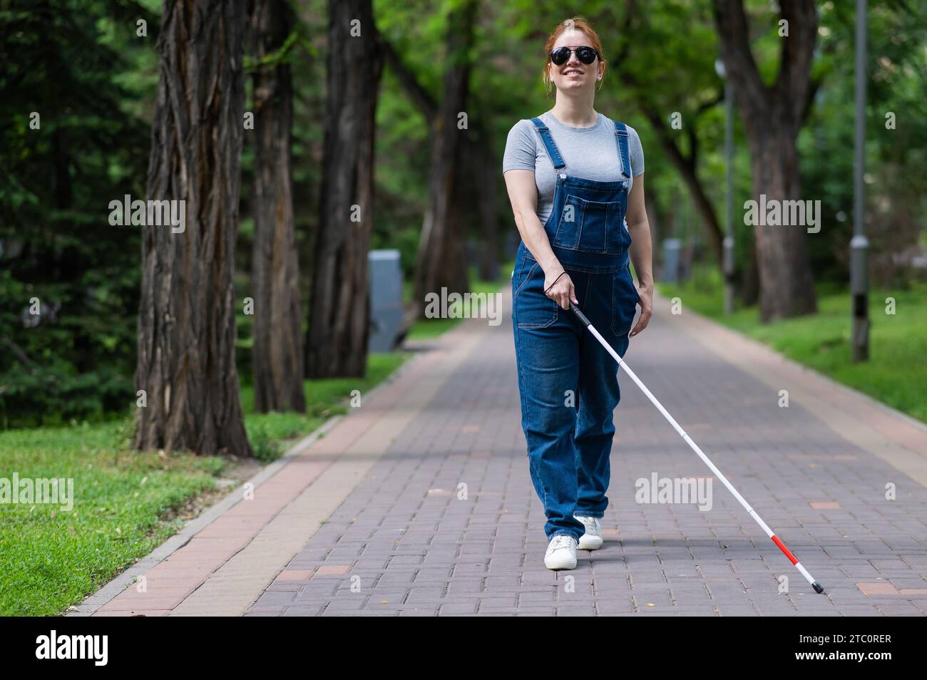 Blinde schwangere Frau, die mit einem Stock im Park spaziert. Stockfoto