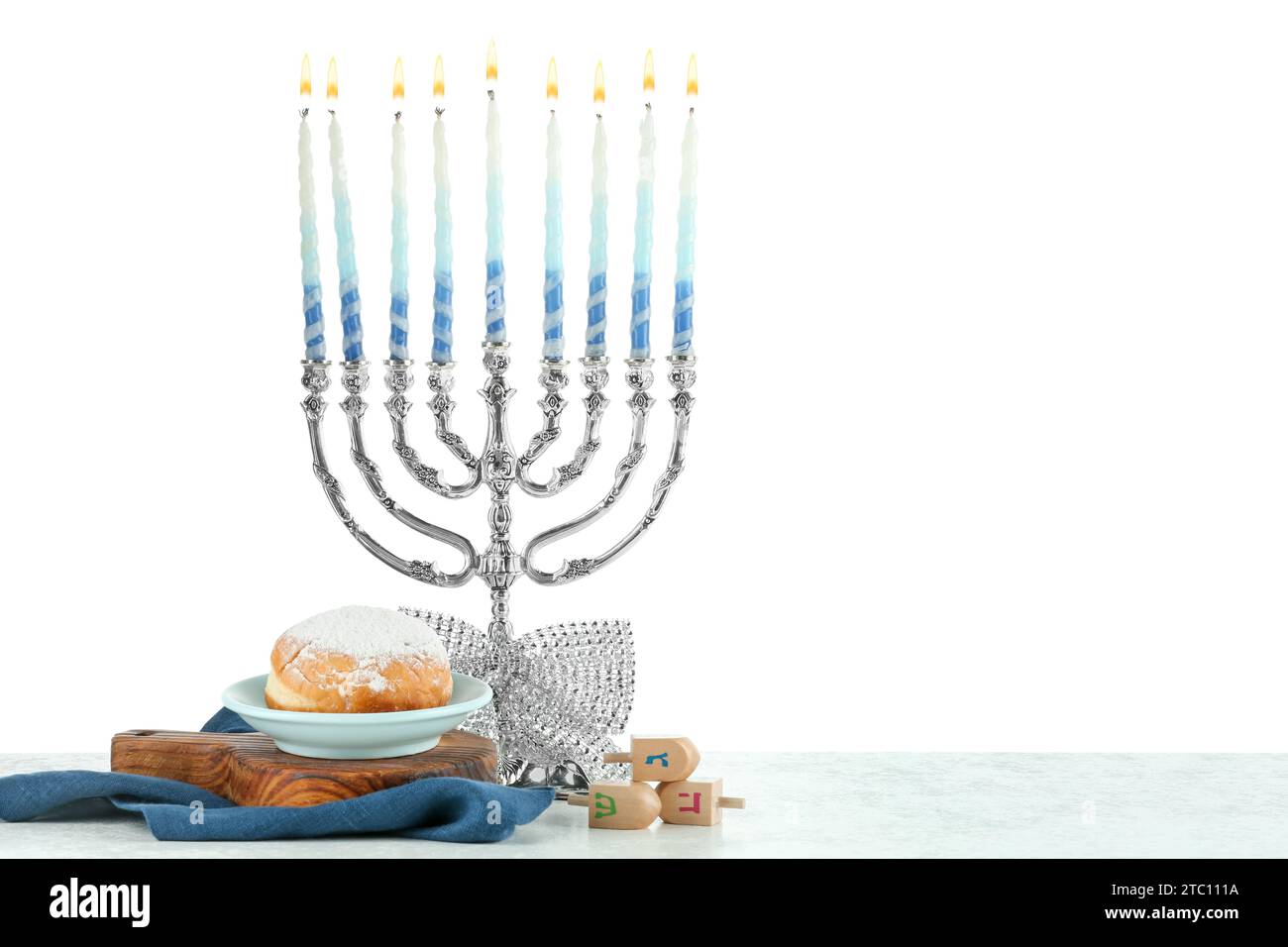 Hanukkah-Feier. Menora mit bunten Kerzen, Dreidels und Donuts auf weißem Hintergrund Stockfoto