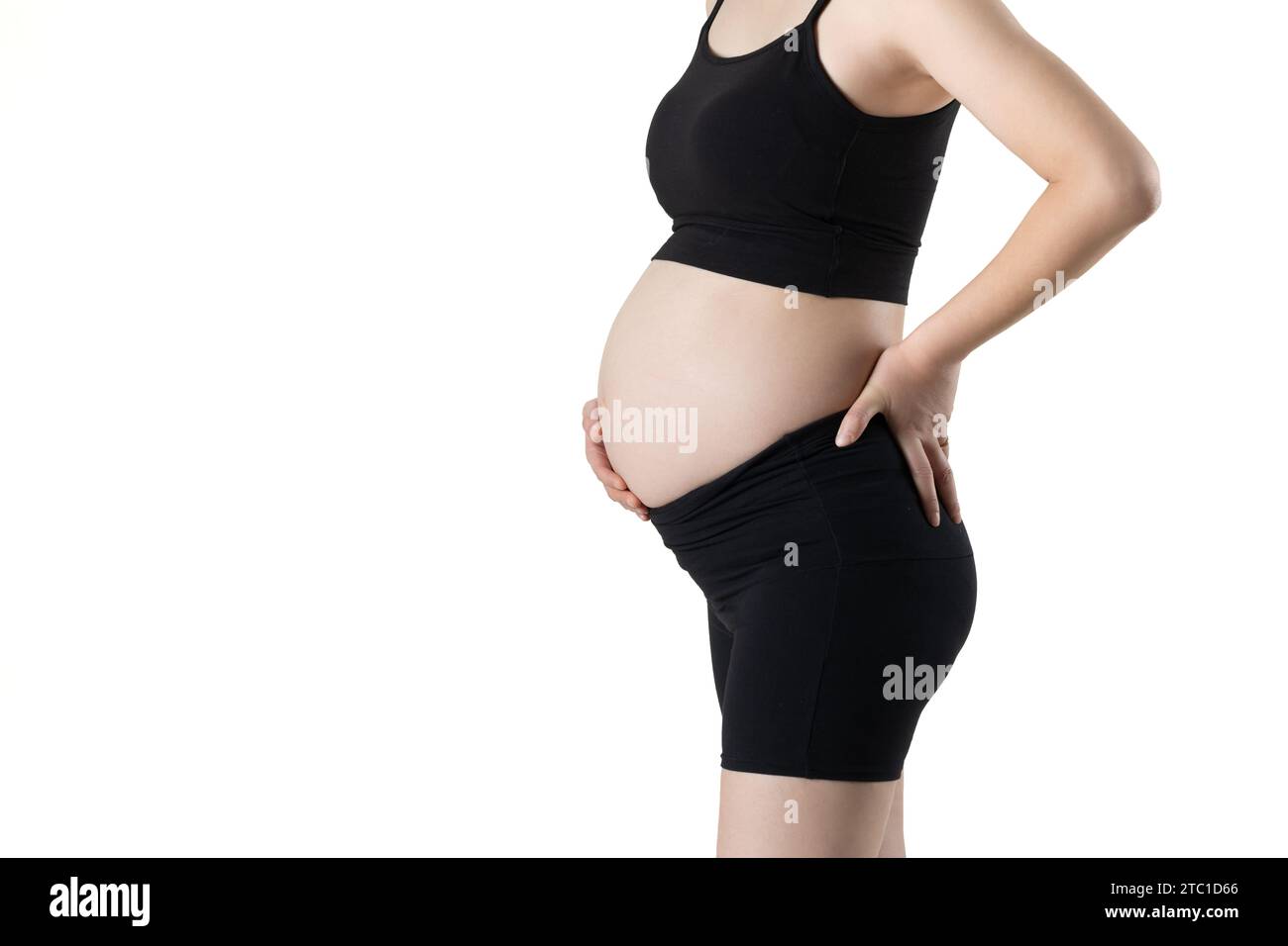 Schwangere Frau, die ihren Bauch herausstreckt und ihn mit den Händen bedeckt (isoliert auf weißem Hintergrund) Stockfoto