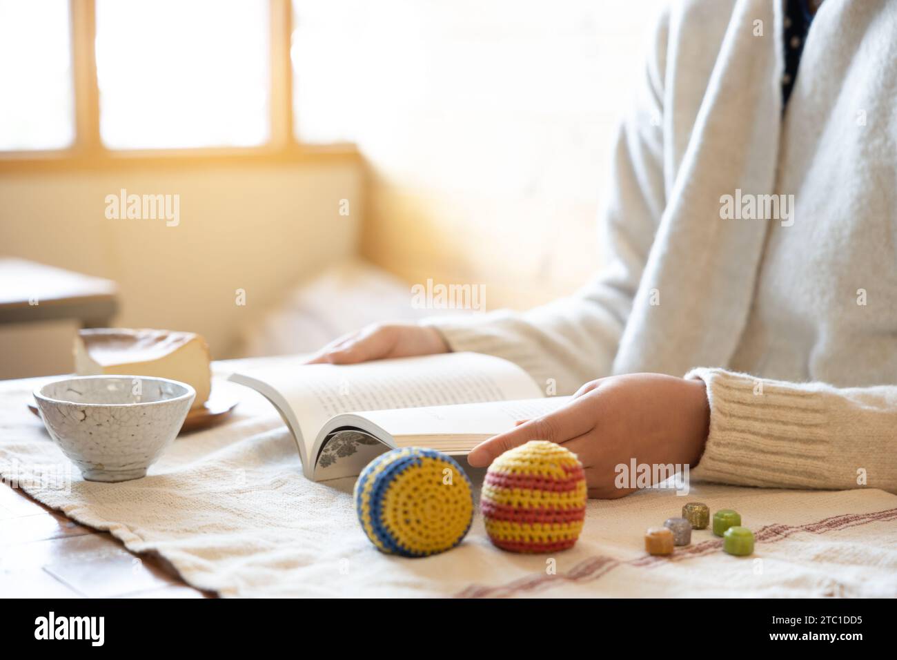 Eine Frau liest ein Buch, es gibt Spielartikel und Teetasse auf dem Tisch, ohne Fokus Stockfoto