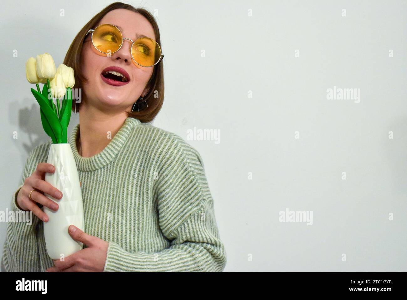Ein Porträt einer jungen kaukasischen Frau, die eine Vase weißer Tulpen hält. Stockfoto