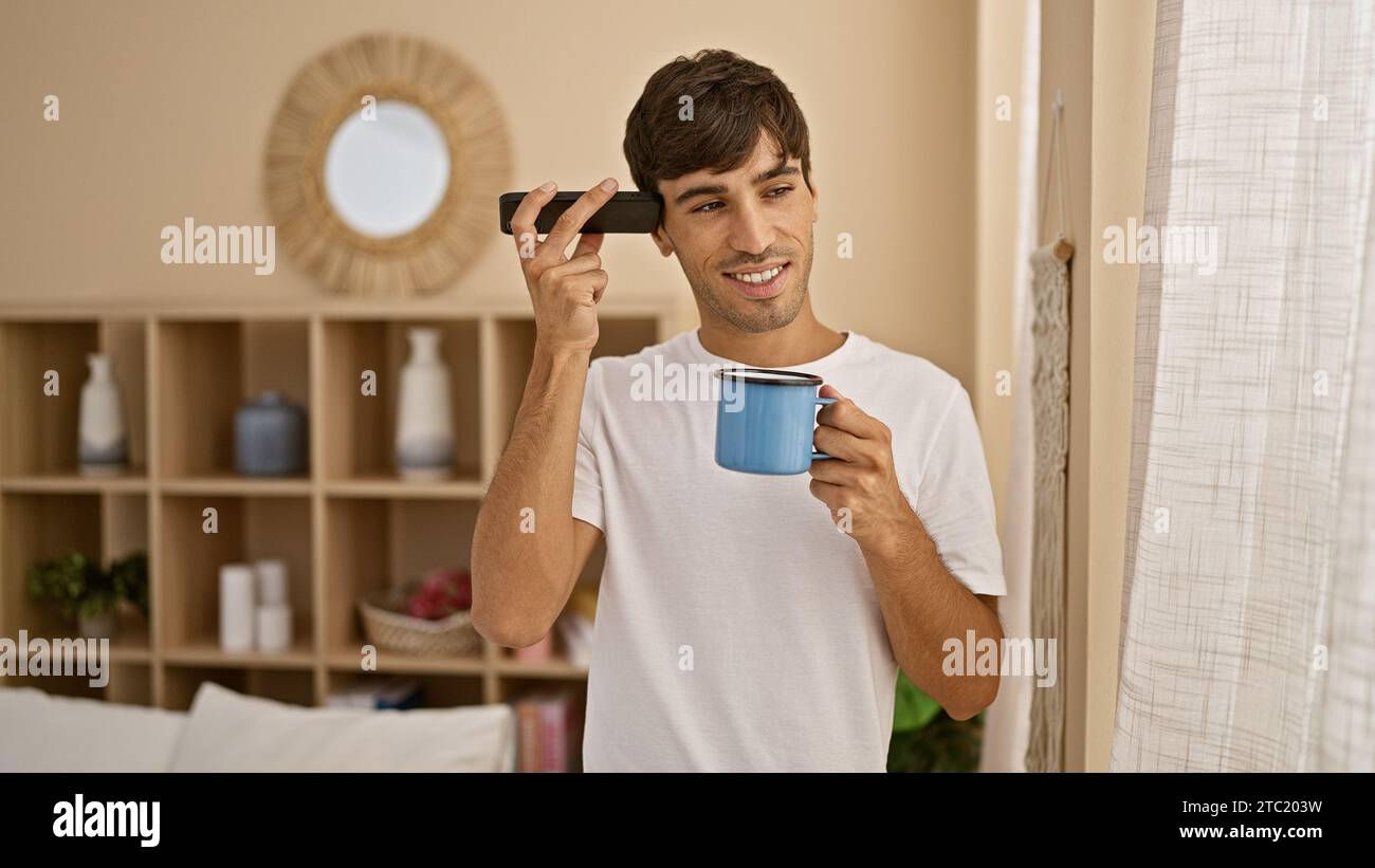 Entspannter Morgen, lächelnder, gutaussehender junger hispanischer Mann, der sich zu Hause entspannt und eine heiße Tasse Kaffee genießt, während er einem fesselnden voi lauscht Stockfoto Entspannter Morgen, lächelnder, gutaussehender junger hispanischer Mann, der sich zu Hause entspannt und eine heiße Tasse Kaffee genießt, während er einem fesselnden voi lauscht Stockfoto