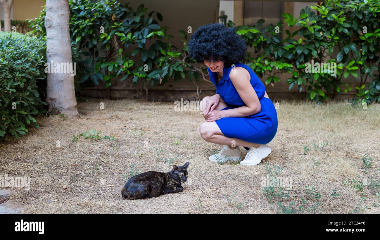 Frau mit lockigen schwarzen Haaren und einer streunenden Katze auf der Straße. Stockfoto