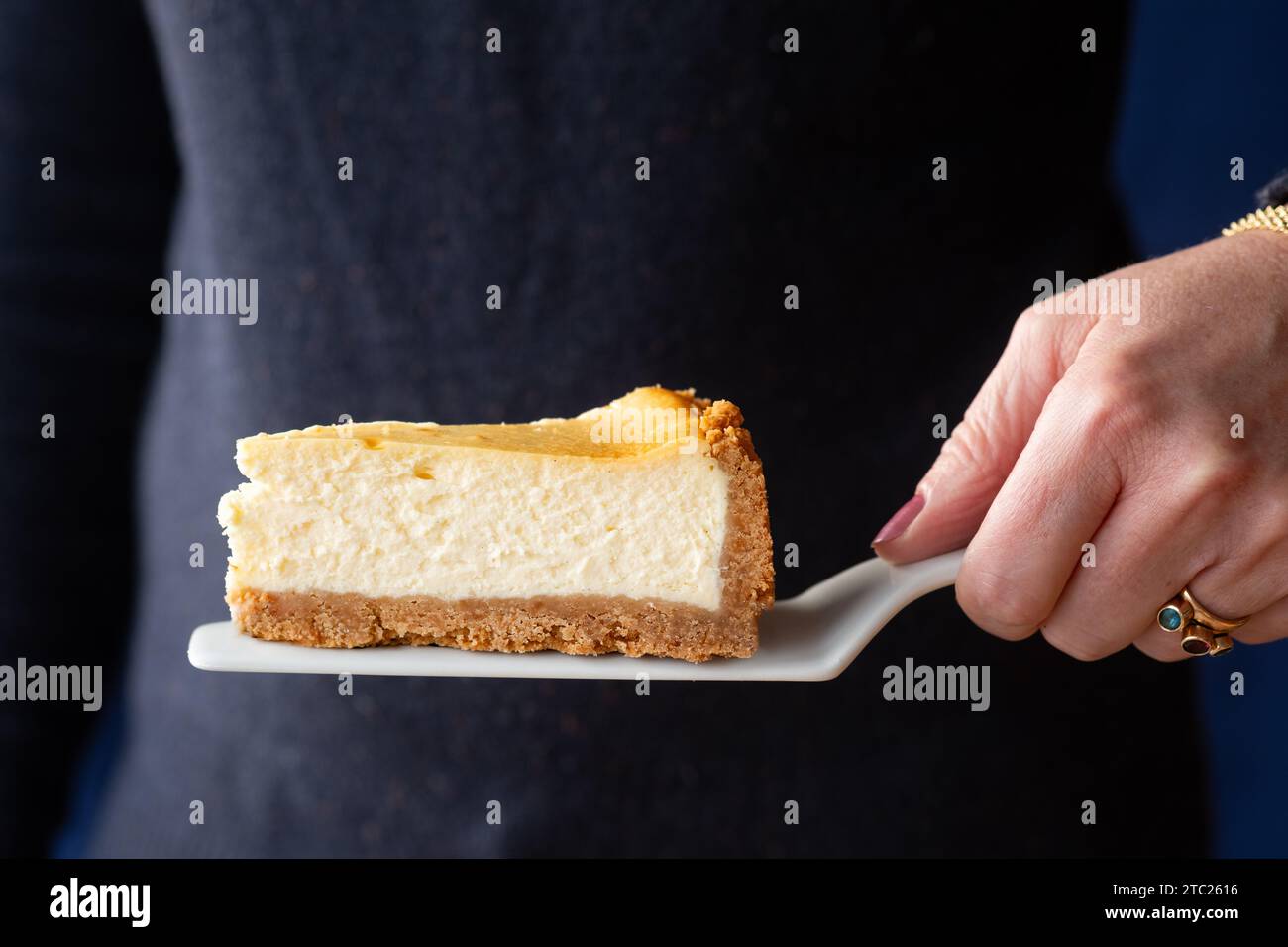 Eine Frau, die eine tiefe, köstliche Portion New Yorker Käsekuchen auf einer Kuchenscheibe hält Stockfoto