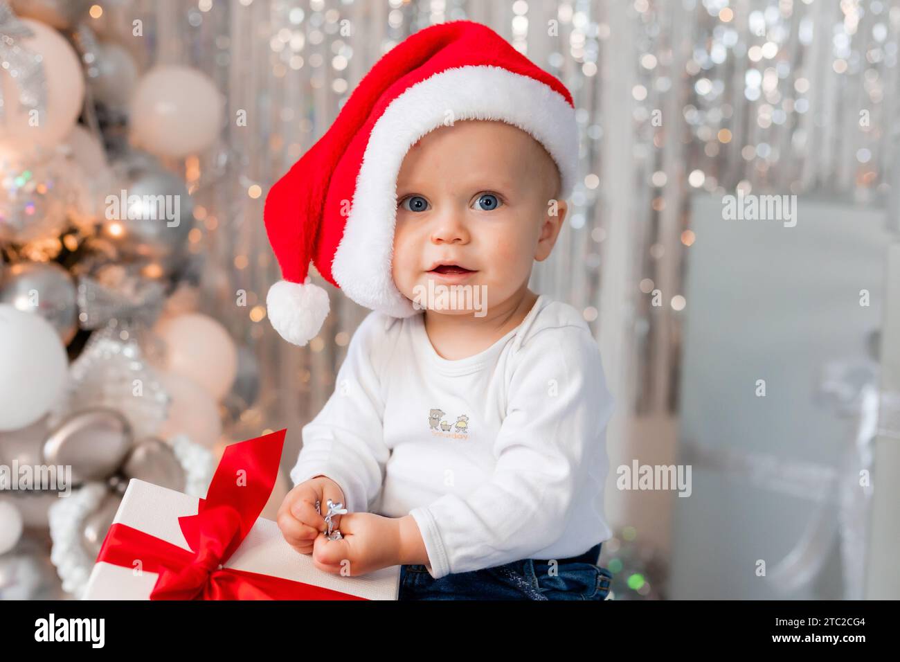 Süßer Junge mit Geschenken am Weihnachtsbaum, kleiner Weihnachtsmann Stockfoto