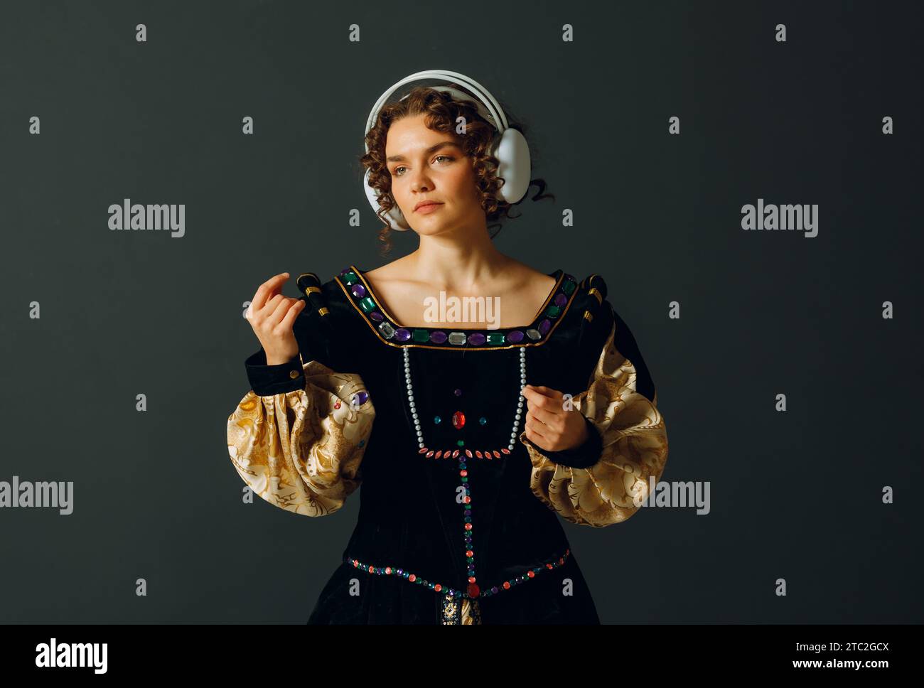 Porträt einer jungen Aristokratin mit Kopfhörern auf dem Kopf und mittelalterlichem Kleid lauscht klassischer Musik Stockfoto