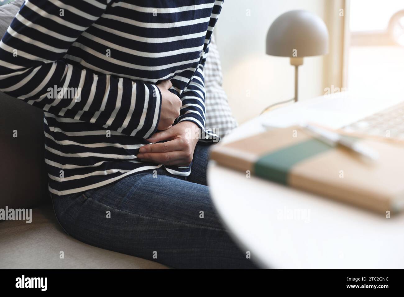 Junge Frau, die zu Hause unter Magenschmerzen leidet, Nahaufnahme. Lebensmittelvergiftung, Krämpfe Stockfoto