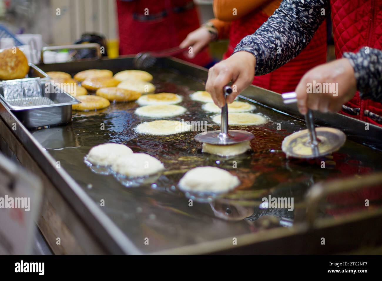 Eine Frau presst auf einem traditionellen koreanischen Markt Hotteok-Teig fachmännisch in sibelndes Öl und zeigt die Kunst, dieses beliebte Street Food herzustellen. Stockfoto