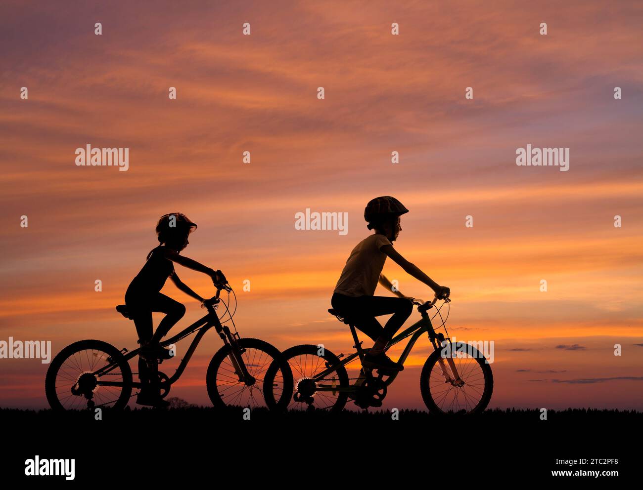Silhouetten zweier fahrradfahrender Mädchen vor dem Hintergrund des Sonnenuntergangs Stockfoto