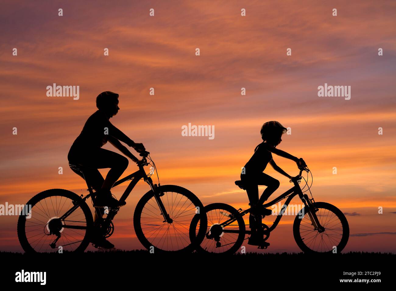 Silhouetten einer Frau und eines kleinen Mädchens auf Fahrrädern vor dem Hintergrund des Sonnenuntergangs Stockfoto
