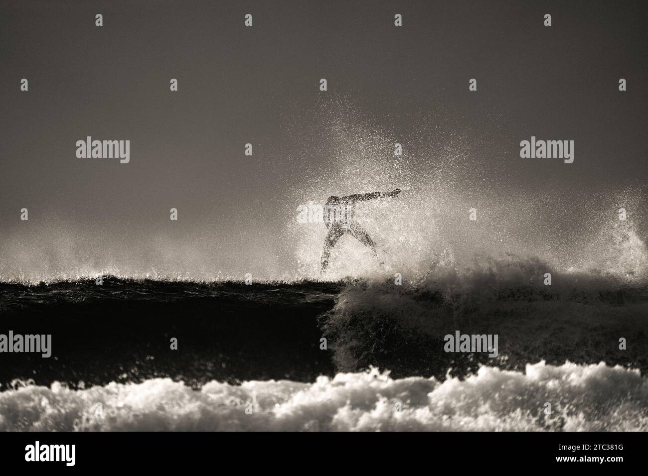Surfer im Hintergrund, der eine Silhouette gegen das goldene Leuchten der untergehenden Sonne schmiegt. Eine künstlerische Szene, in der die Leidenschaft für das Surfen festgehalten wird Stockfoto