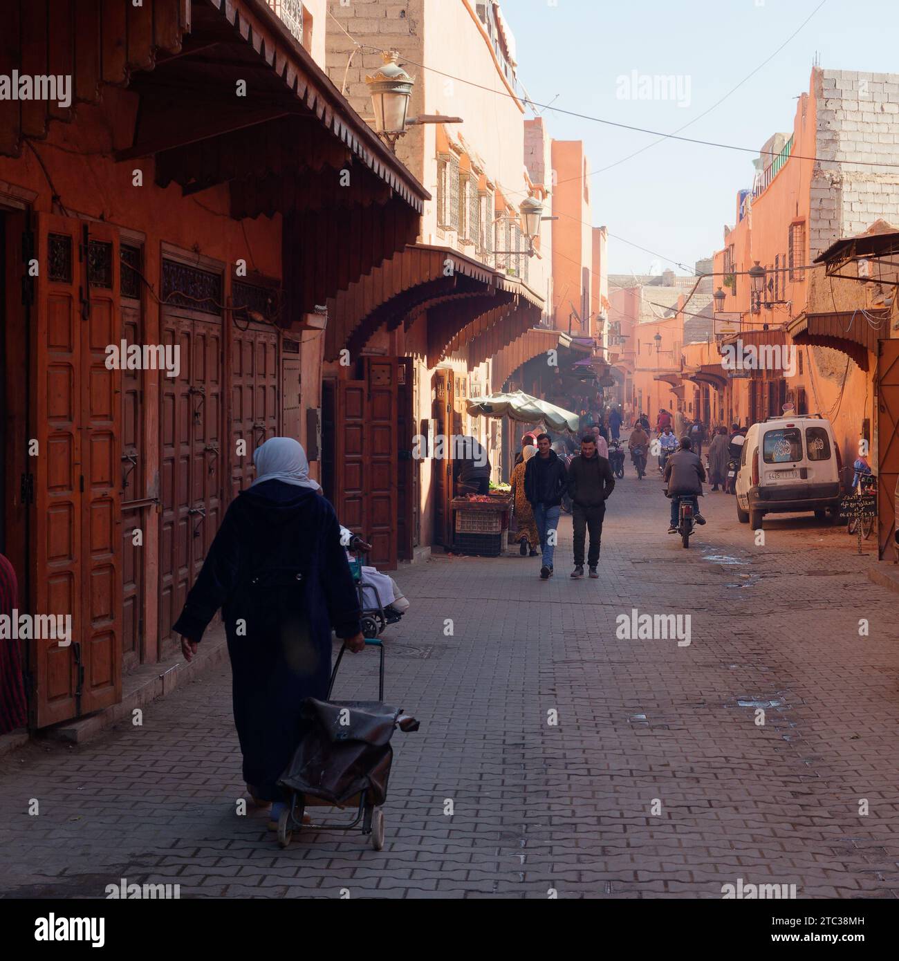 Lady läuft eine Straße mit Einkaufswagen in der Stadt Marrakesch aka Marrakesch mit Moschee in der Ferne, Marokko, 10. Dezember 2023 Stockfoto
