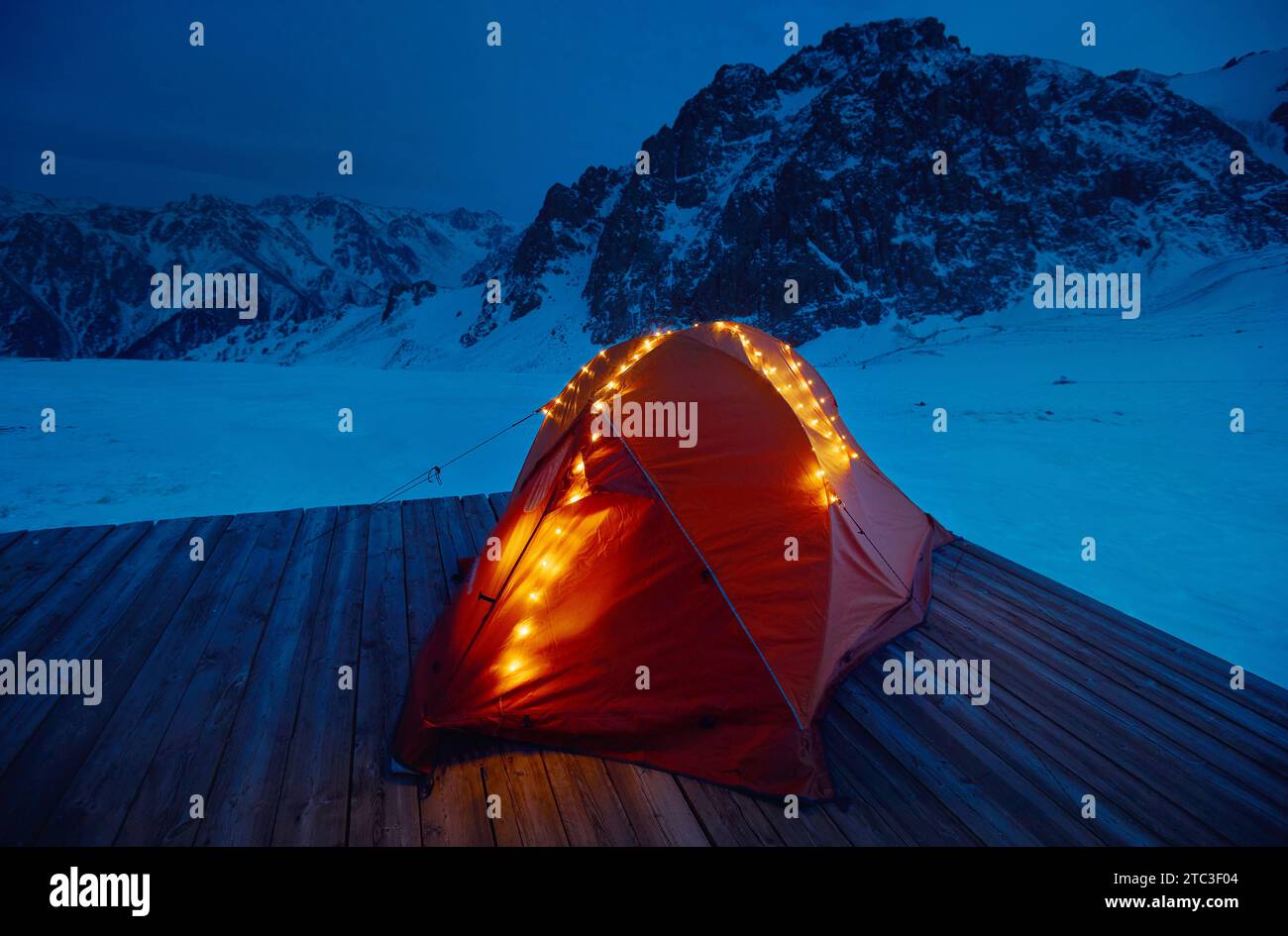 Oranges Touristenzelt auf dem Campingplatz mit leuchtenden Weihnachtsgirlanden Lichtern in den Winterbergen bei Nacht Stockfoto