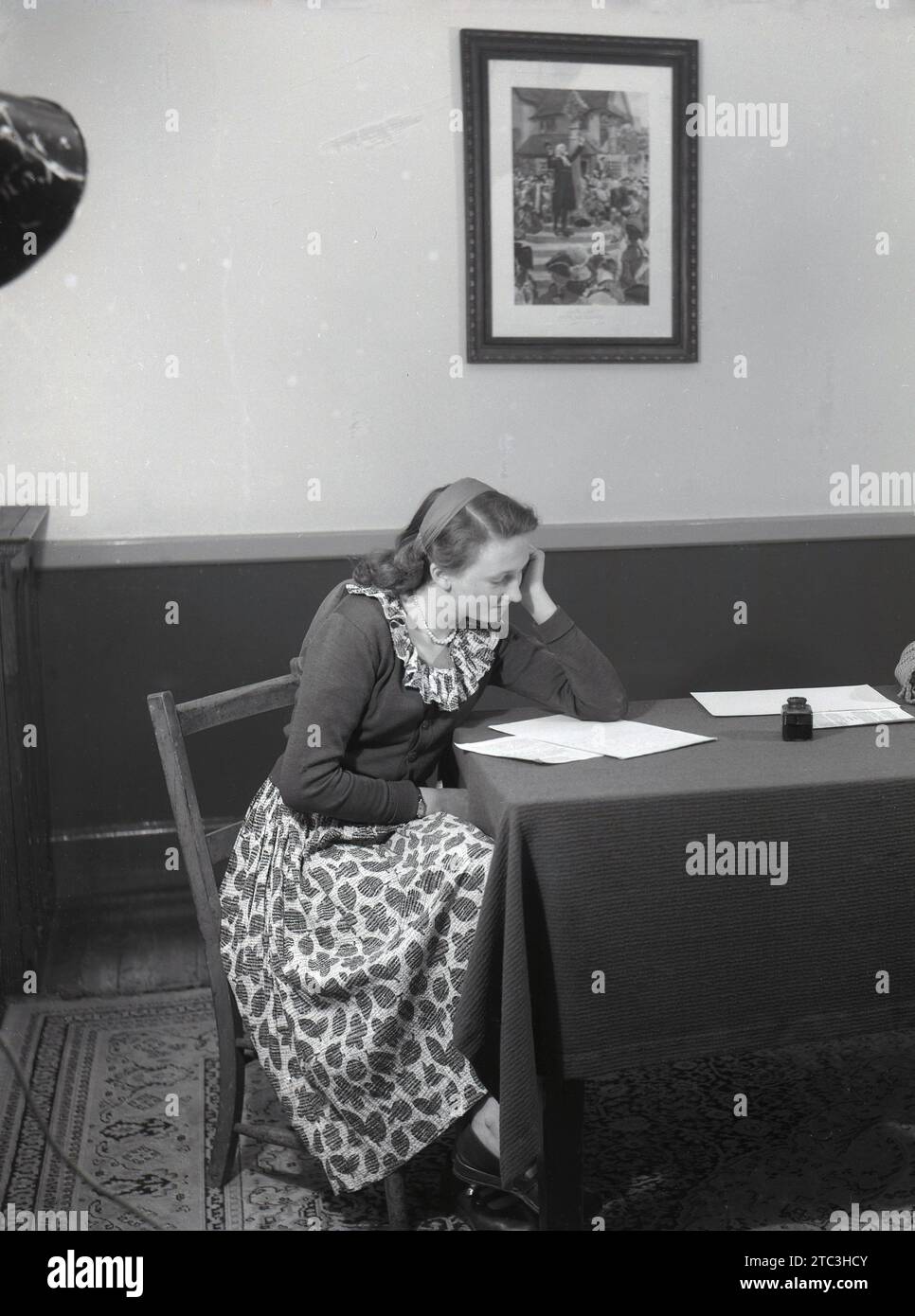 1950er Jahre, historisch, eine junge Dame sitzt an einem mit Stoff bedeckten Tisch und liest handgeschriebene Manuskripte. Stockfoto