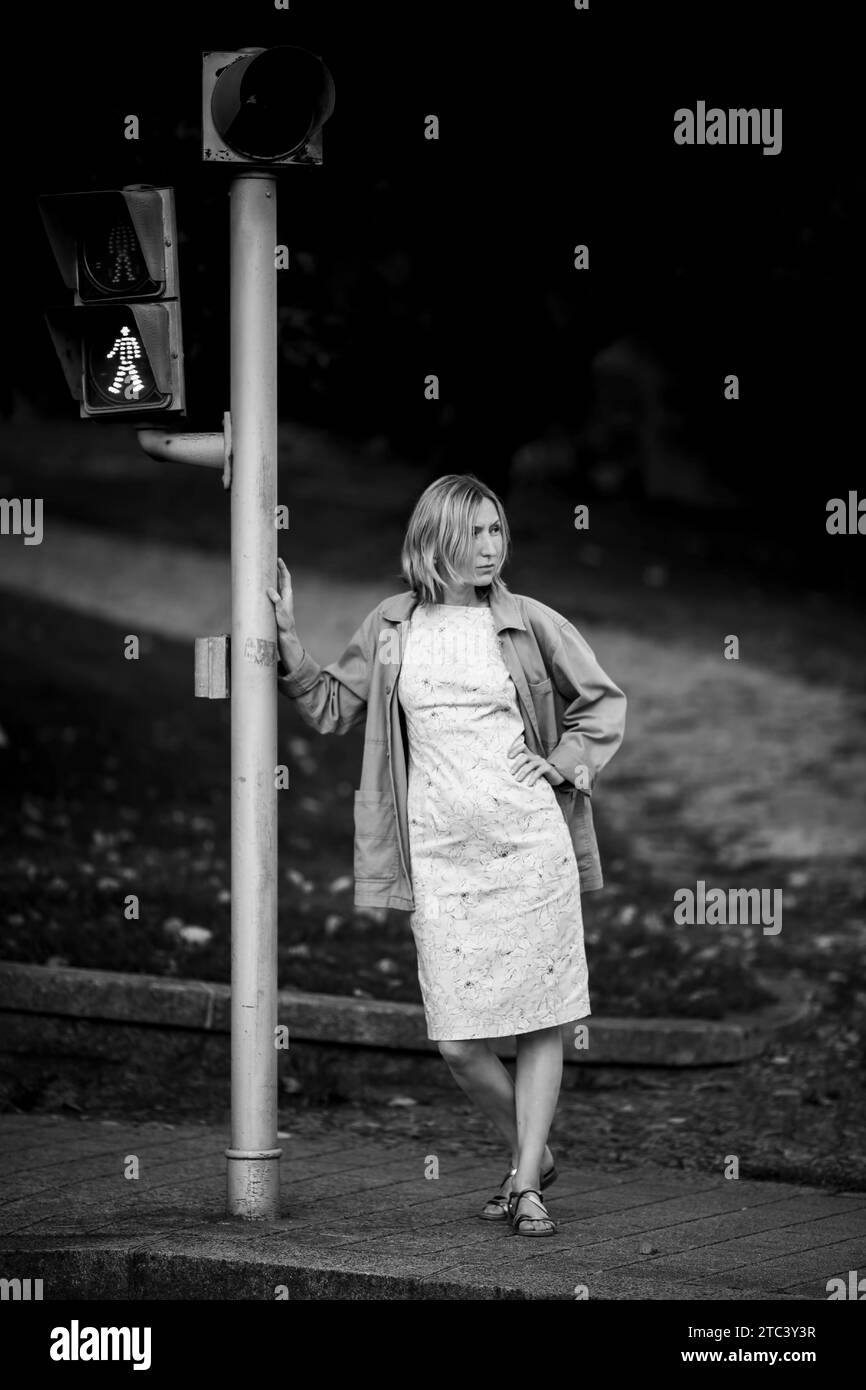 Eine Frau, die neben einer Ampel an einem Straßenübergang steht. Schwarzweißfoto. Stockfoto