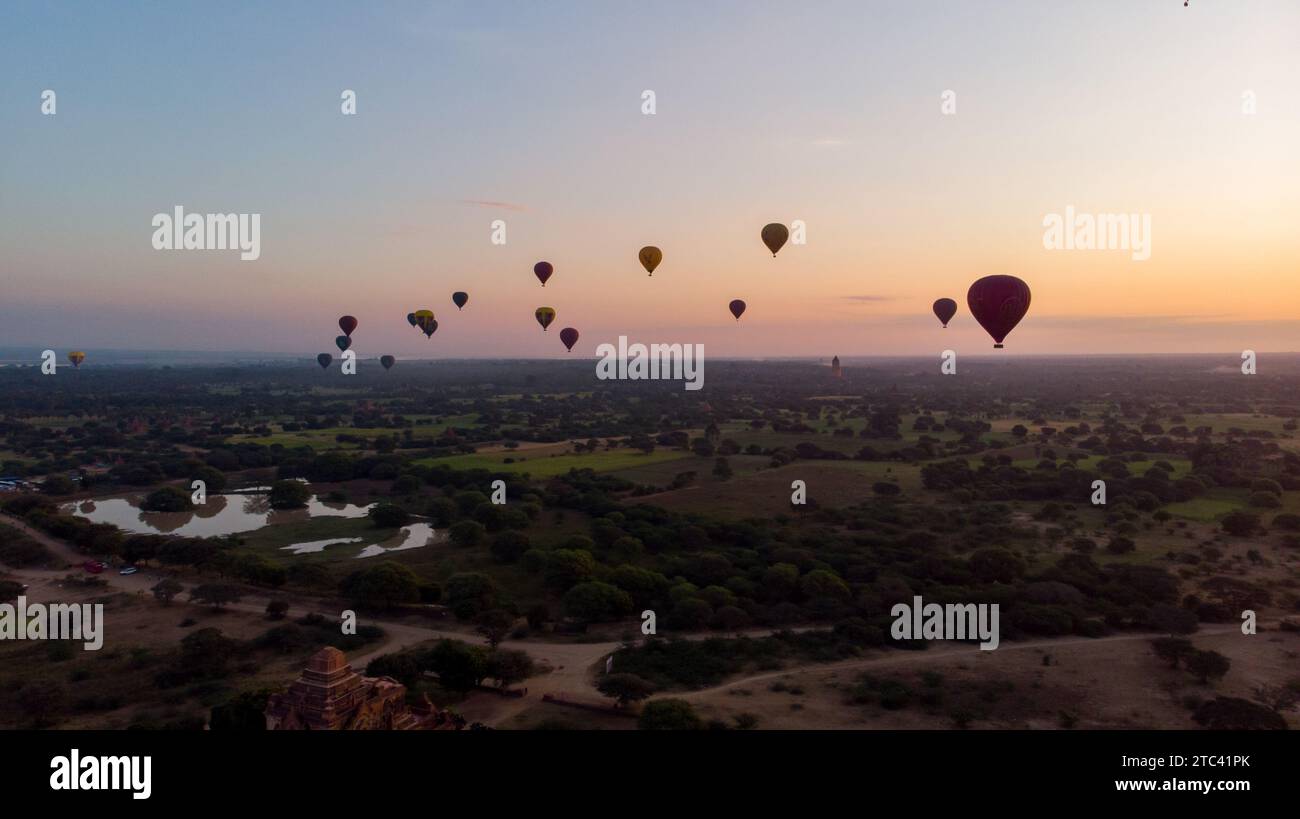 Ein atemberaubendes Bild einer Schar Heißluftballons, die über eine Landschaft mit üppigen Bäumen schweben und eine wunderschöne Himmelslandschaft schaffen Stockfoto
