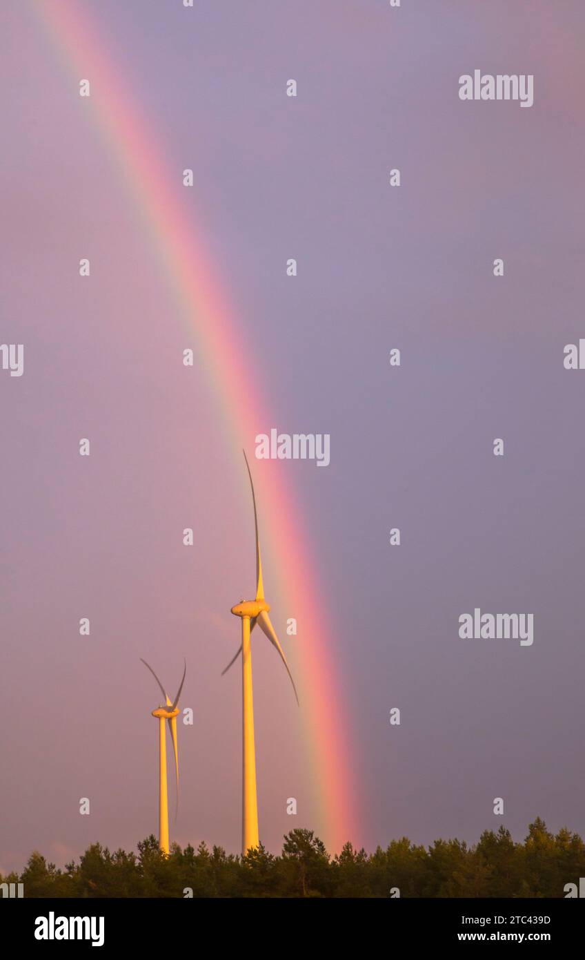 Ein lebhafter und farbenfroher Regenbogen überbrückt den Himmel über einem malerischen Windpark, der mit surrenden Windturbinen gefüllt ist Stockfoto
