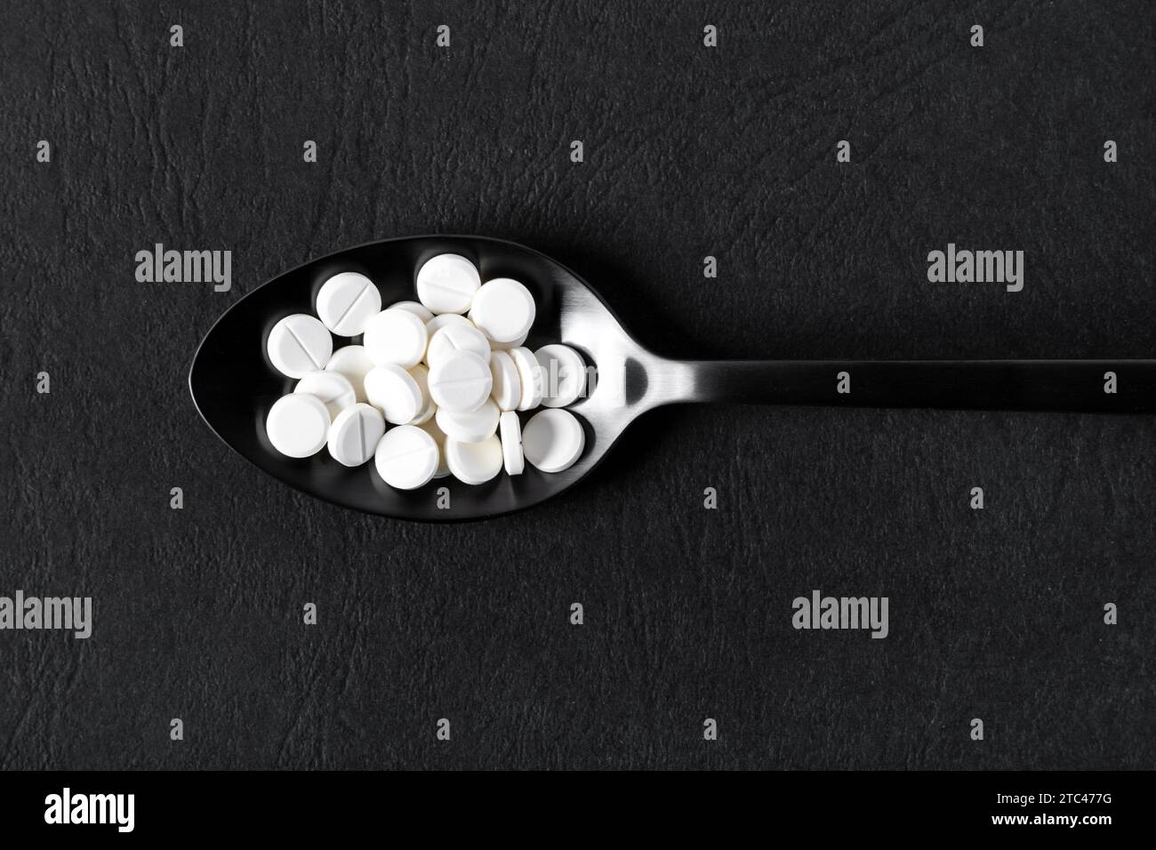 Weiße Tabletten auf einem schwarzen Löffel Stockfoto