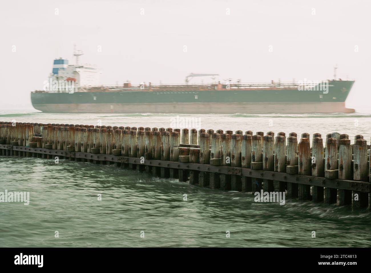 Großes Tankschiff, das auf See mit Bewegungsunschärfe segelt, vorbei am Wellenbrecher am Hafen eines Hafens Stockfoto