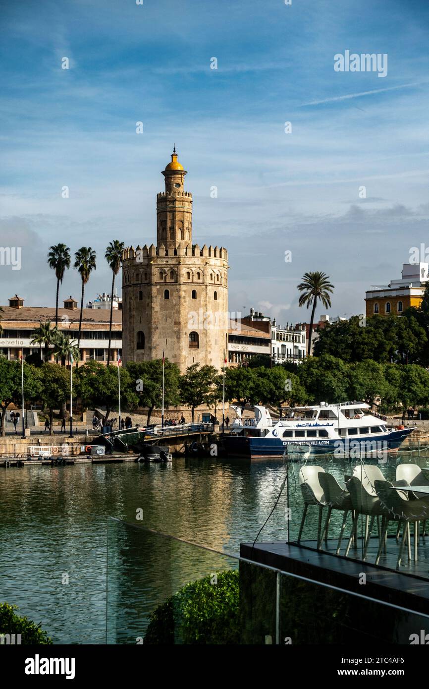Der historische Torre del Oro steht hoch neben dem Fluss Guadalquivir mit Palmen und einem Boot in Sevilla., Spanien. Stockfoto