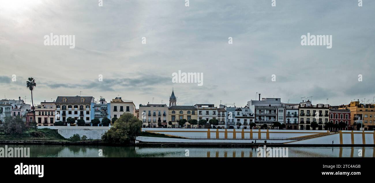 Sevillas malerischer Flussufer, gesäumt von klassischer andalusischer Architektur unter einem stimmungsvollen Himmel. Stockfoto