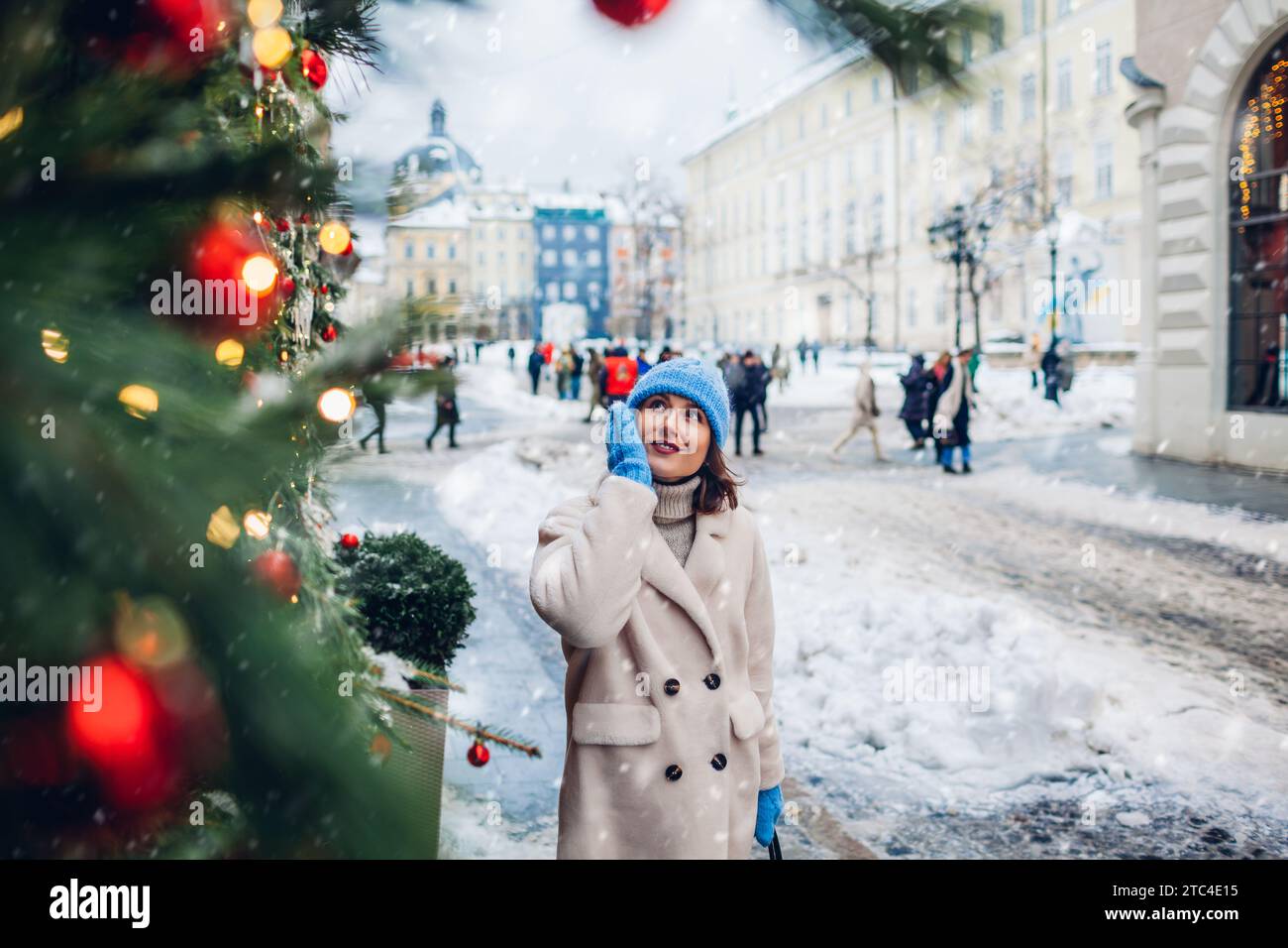 Porträt einer stilvollen Frau, die auf der zu Weihnachten dekorierten Stadtstraße unter fallendem Schnee läuft und Architektur genießt. Wintermode Stockfoto