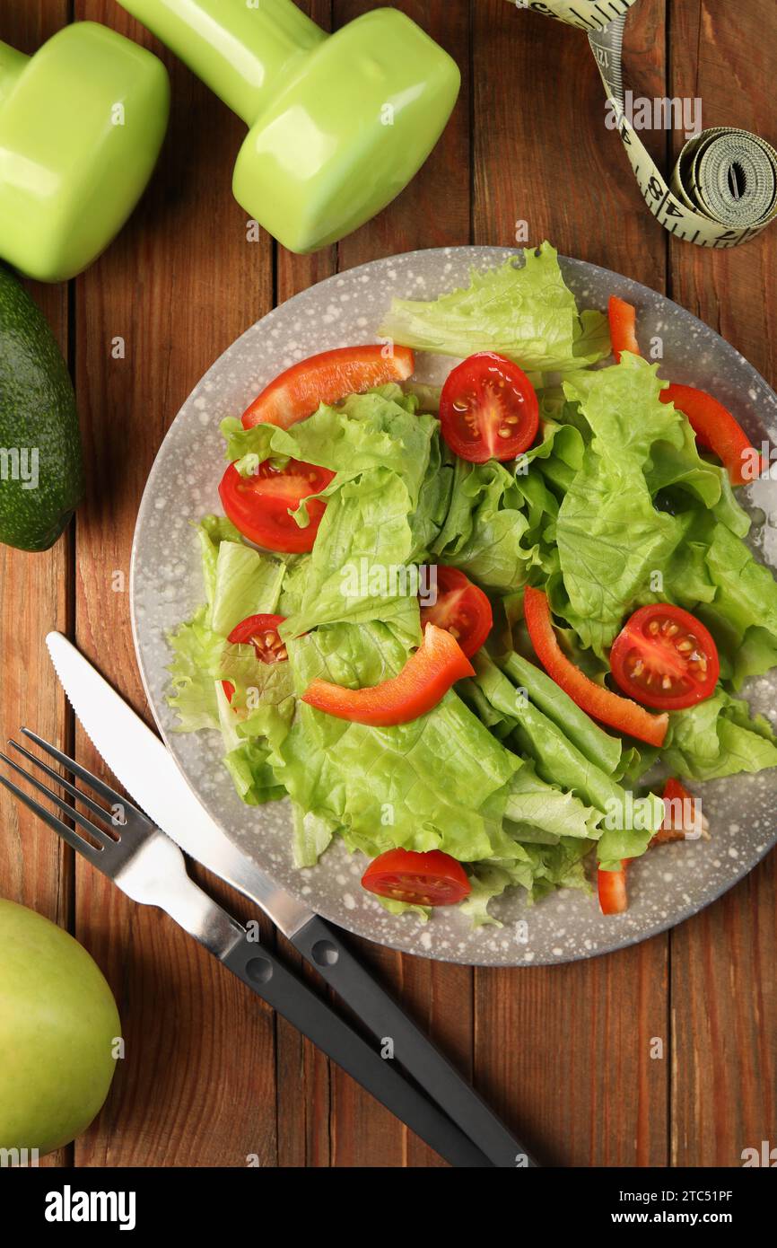 Gesunde Ernährung. Salat, Besteck, Kurzhanteln und Maßband auf Holztisch, flach gelegt Stockfoto
